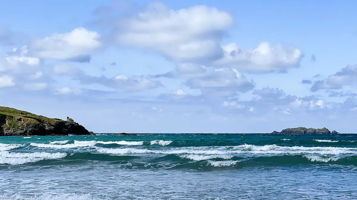 Waves rolling into Harlyn Bay under a sky of white clouds