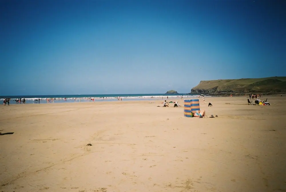 Families on the wide sands of Polzeath beach under a deep blue sky