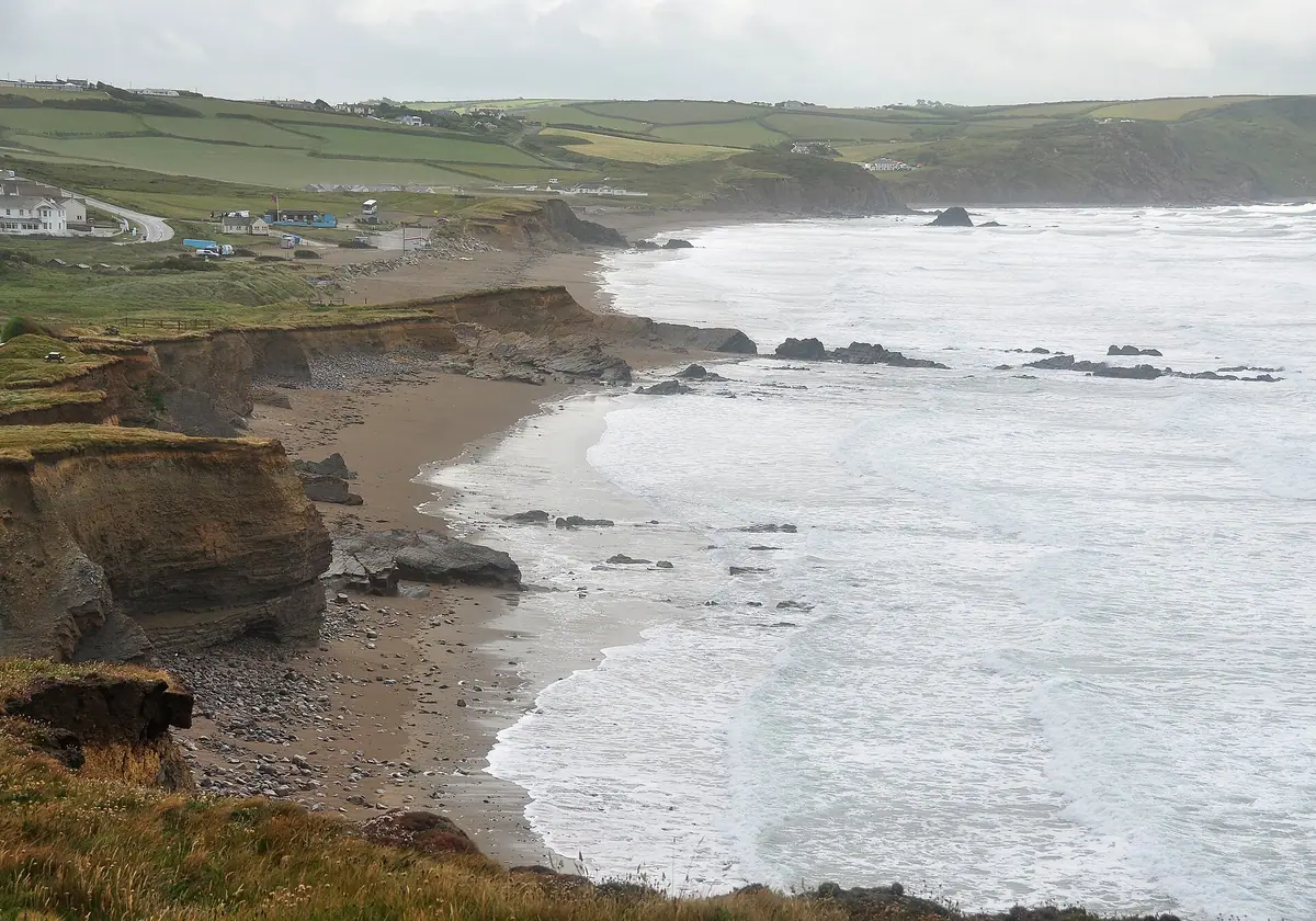 Waves breaking along Widemouth Bay with low cliffs and farmland behind